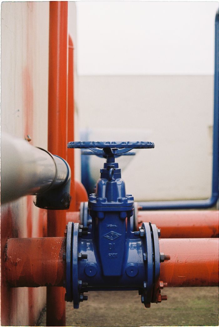 services-01 Close-up of a blue gate valve on red pipes, showcasing industrial plumbing.