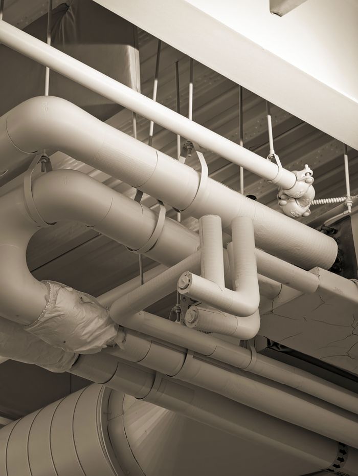 ours-journey Complex network of industrial pipes and ducts in a sepia-toned indoor setting.