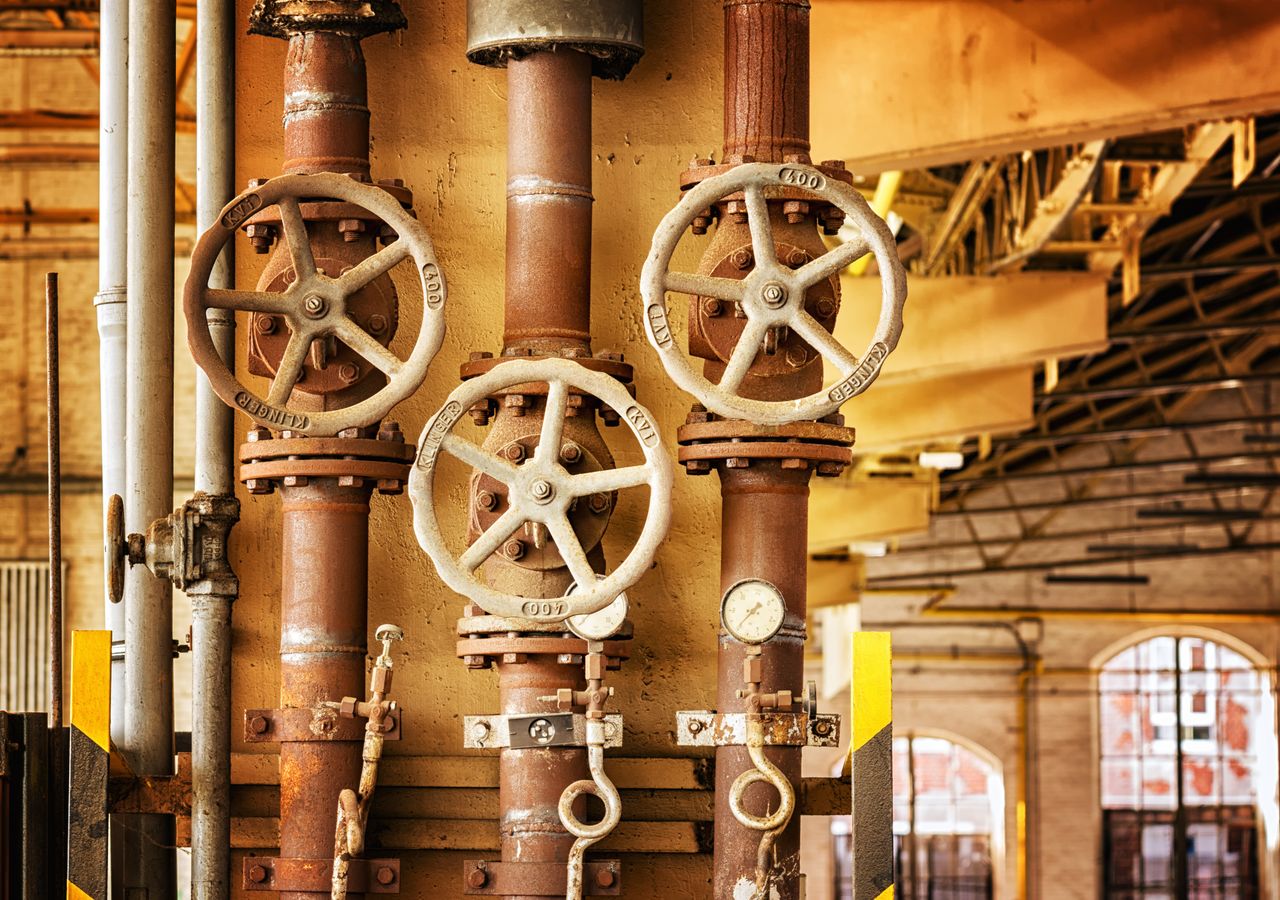 services-04 Close-up of rusty industrial pipes and valves, showcasing aging machinery in a factory setting.