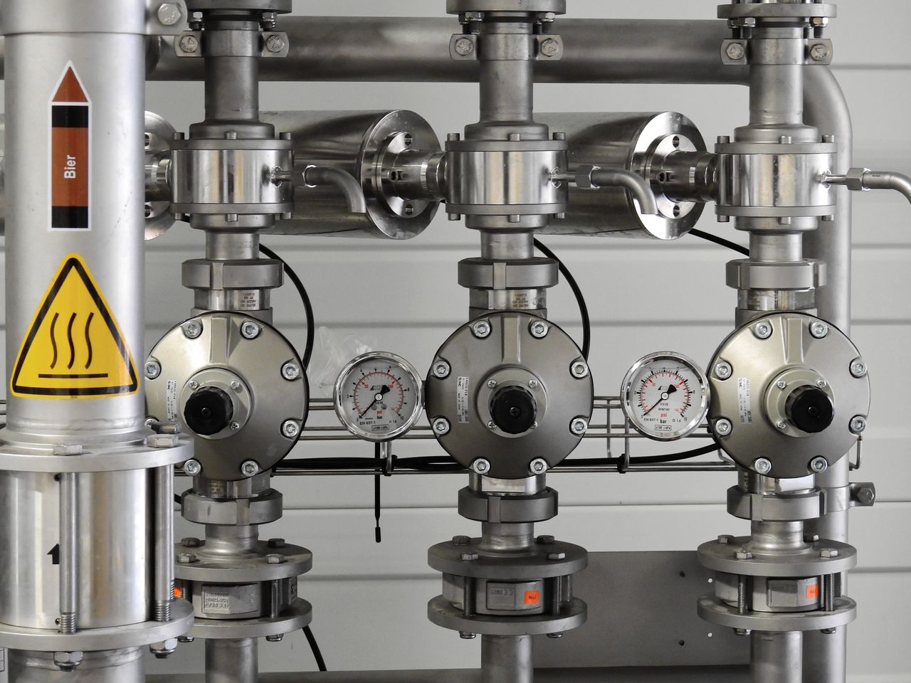 hero-img-01 Close-up of stainless steel pipes with pressure gauges in an industrial setting.