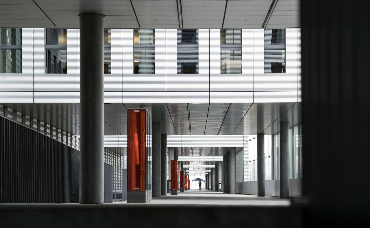 about-img A perspective view down a modern architectural corridor in Basel, featuring geometric patterns and natural light.